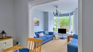 Een woonkamer met een blauwe bank, een houten eettafel met stoelen, een televisie en een kroonluchter.