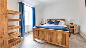 Une chambre à coucher avec un lit en bois, deux tables de chevet, une commode, une fenêtre avec des rideaux et un luminaire au plafond.