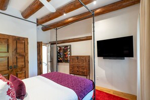 A bedroom with a bed, a wooden wardrobe, a television on the wall, and a red carpet.