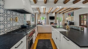 Eine moderne Küche mit Kochinsel, Holzbalken an der Decke und einer dekorativen Spritzschutzwand.