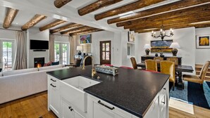 Eine moderne Küche mit einer zentralen Kochinsel, Holzbalken, einem Essbereich mit Stühlen und einem Kamin.