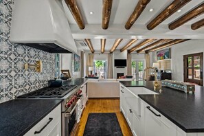 A modern kitchen with a central island, wooden ceiling beams, and patterned backsplash.