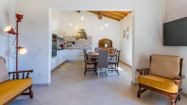 A modern kitchen with white cabinets, a dining area with wooden chairs, and a large flat-screen TV mounted on the wall. - Beautiful apartment for 7 people with A/C, WIFI and pets allowed (Donoratico)