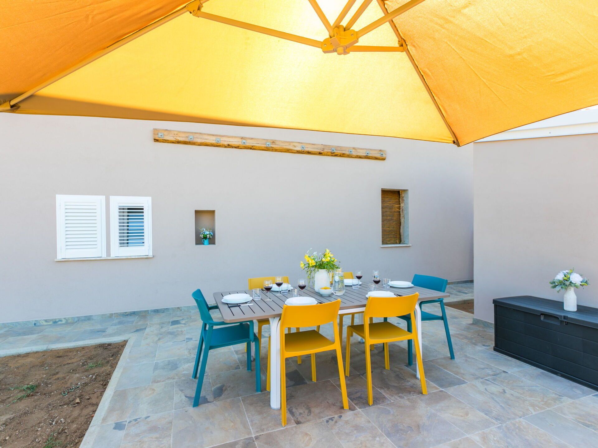 Un patio al aire libre con una mesa dispuesta para comer, rodeado de sillas, bajo un amplio toldo.