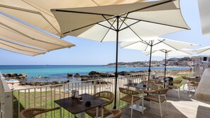 A terrace with wicker chairs and tables, overlooking a beach with clear blue water and rocky outcrops. - Nice apartment for 3 guests with WIFI, A/C, TV and terrace (Porto Torres)