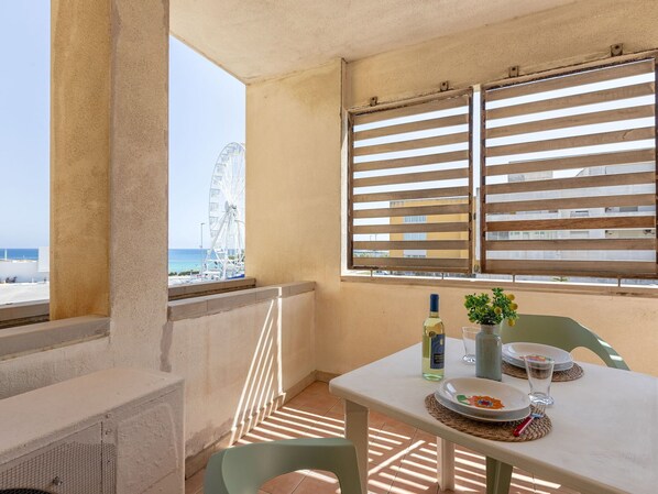 A balcony with a table set for two, a bottle of wine, and a small plant.