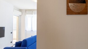 A living room with a blue sofa, a flat-screen TV mounted on the wall, and a wooden artwork. - Nice apartment for 3 guests with WIFI, A/C, TV and terrace (Porto Torres)