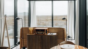 A modern room with a large window, a wooden table, a chair, a radio, and a lamp. - Glass-roof lodge with private spa & sauna near Seljalandsfoss, pure tranquility (Hvolsvöllur)