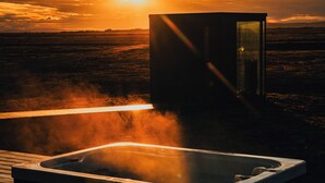 A hot tub on a wooden deck with a sunset in the background. - Glass-roof lodge with private spa & sauna near Seljalandsfoss, pure tranquility (Hvolsvöllur)