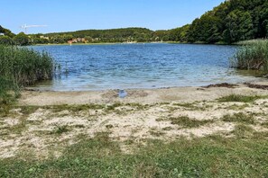 Ein See mit sandigem Ufer und umgebender Bepflanzung.