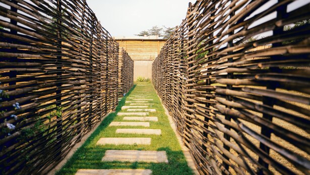 A pathway flanked by bamboo fences leading to a building with a sloped roof. - Migano Residence (Bujumbura)