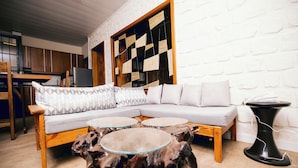 A modern living room with a sectional sofa, round glass tables, and a unique wooden coffee table. - Migano Residence (Bujumbura)