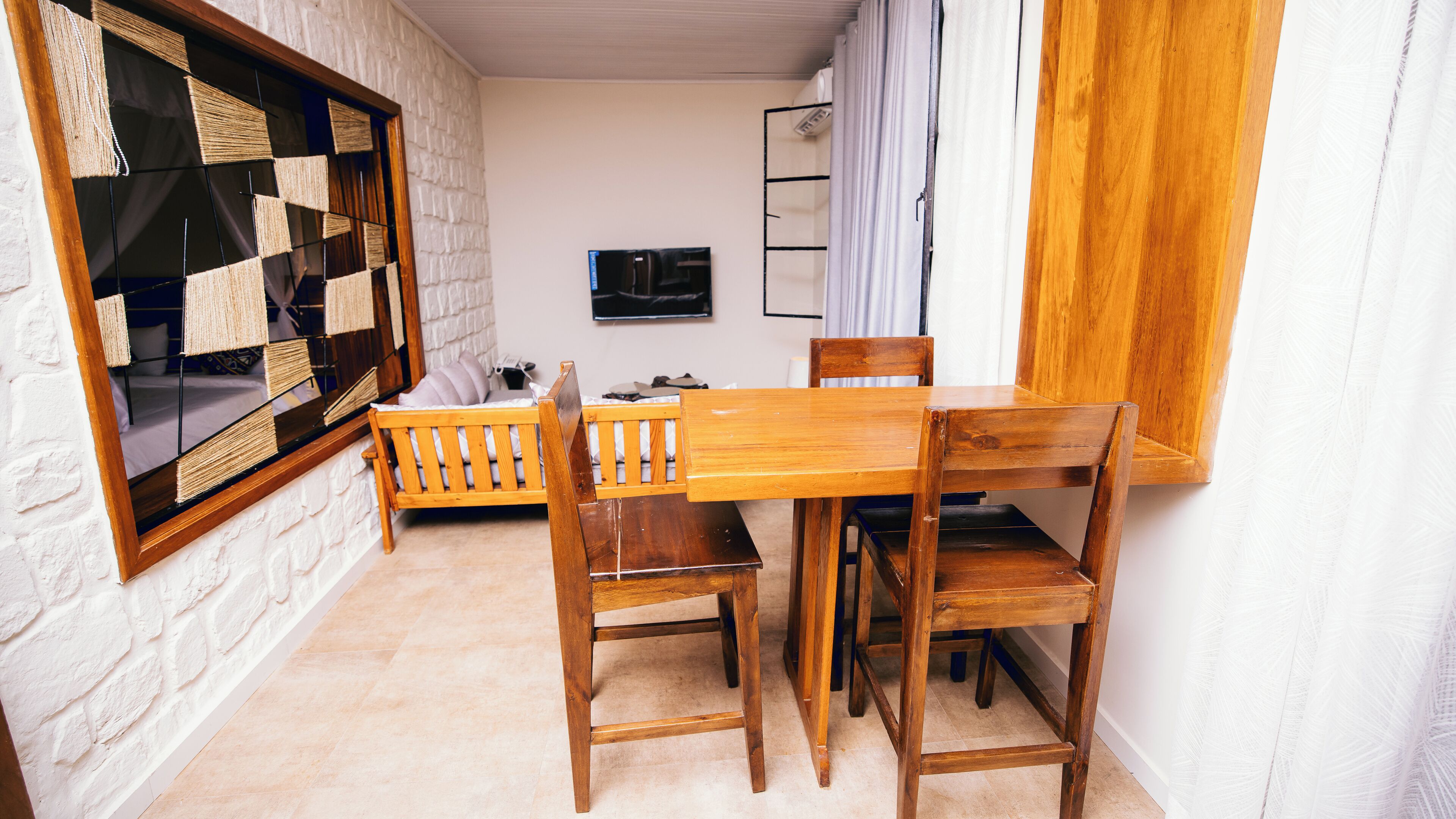 A cozy room with a wooden dining table, two chairs, a small sofa, a TV, and a window with a view of the outside.
