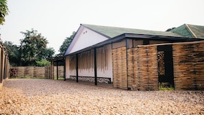 A building with a gravel driveway, a covered walkway, and a fence with vertical slats. - Migano Residence (Bujumbura)