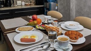 A breakfast table with plates of food, including eggs, sausage, toast, and pastries, along with a coffee cup and a water glass.