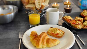 A breakfast setting with croissants, toast, and a glass of orange juice on a table.