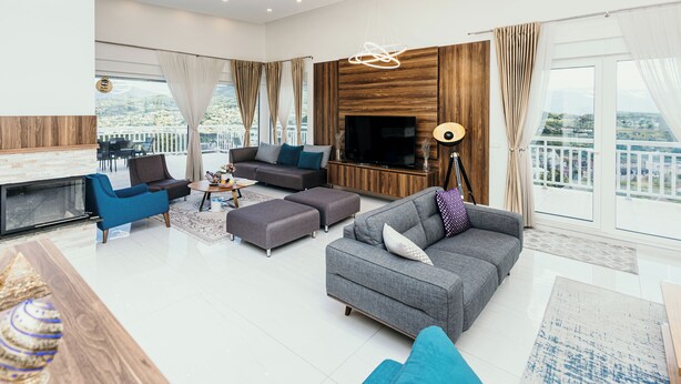 A modern living room with a grey sofa, blue armchairs, a flat-screen TV, and a fireplace.