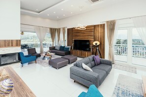 A modern living room with a grey sofa, blue armchairs, a flat-screen TV, and a fireplace. - Sky Rise (Sarajevo)