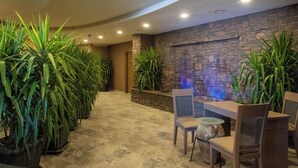 Un hall con pared de piedra, plantas en macetas y un mostrador de recepción con sillas.