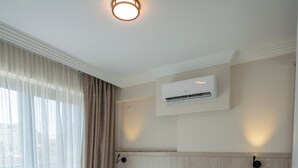 Habitación de hotel con dos camas, una ventana con cortinas, un equipo de aire acondicionado y una lámpara fijada a la pared.