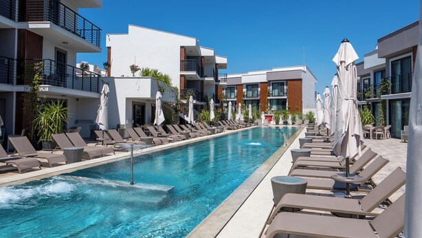 Un hotel moderno con piscina, tumbonas y sombrillas.