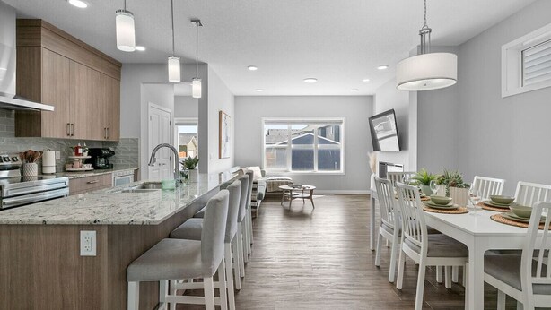 A modern kitchen with a central island, white dining chairs, and pendant lighting.