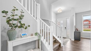 A staircase with white railings leading to a landing with a console table holding a potted plant, a framed picture, and a small box.