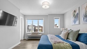 A modern bedroom with a large bed, a bench by the window, and a TV on the wall.