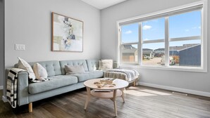 A living room with a light blue sofa, a round coffee table, and a large window with a view of a residential area.