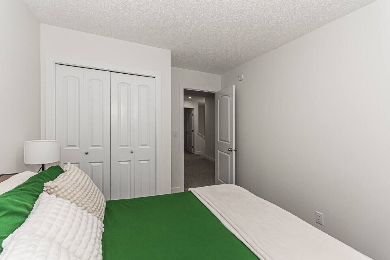 Een hotelkamer met een bed, nachtkastje, lamp en kast.