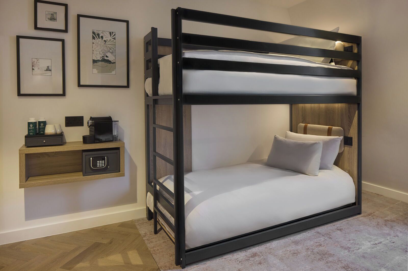 A bunk bed with a wooden headboard, a bedside table with a coffee machine, and framed artwork on the wall.