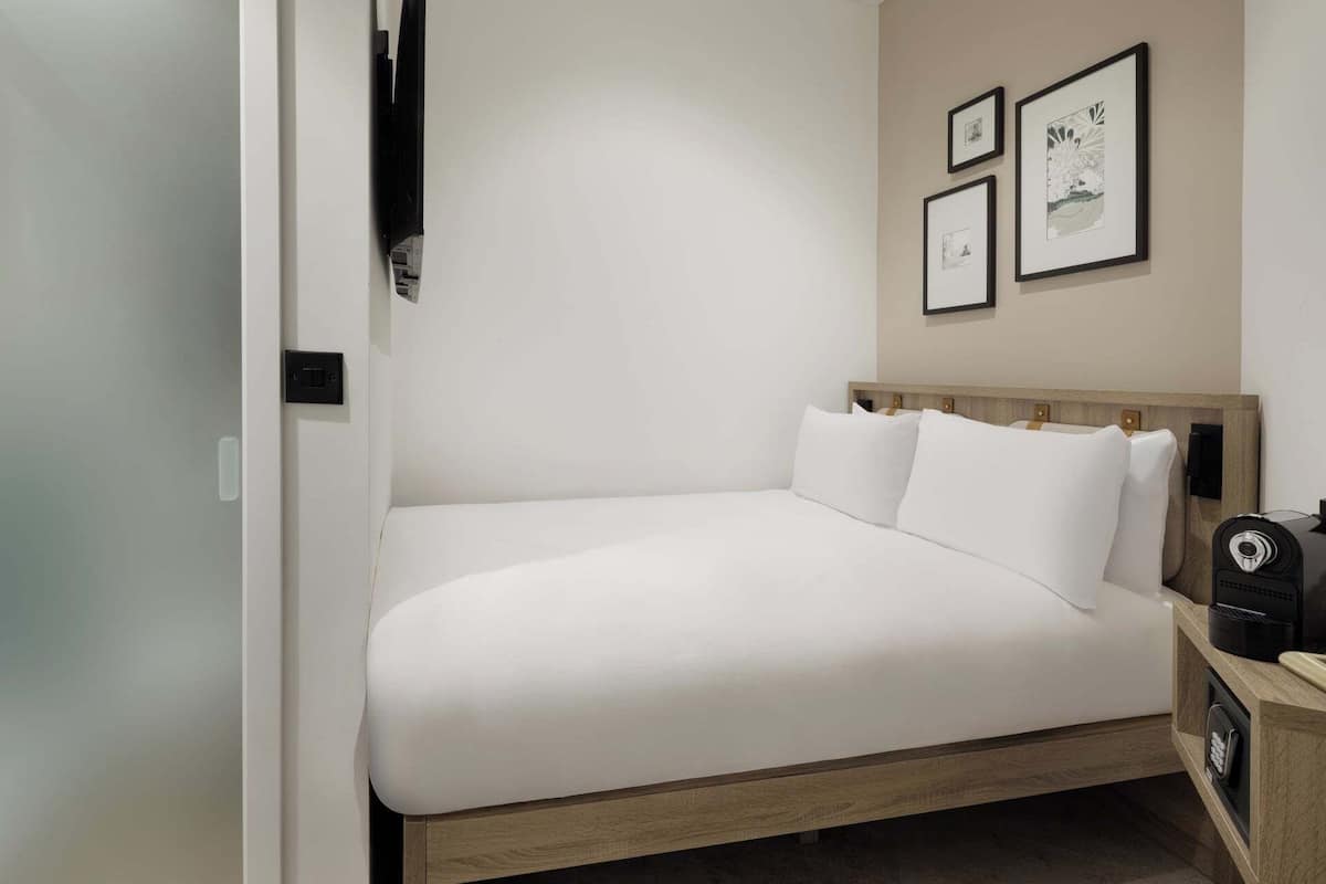 A neatly made bed with white linens in a modern room with a wooden headboard. There are three framed artworks on the wall above the bed.