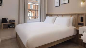 Ein Hotelzimmer mit einem großen Bett, einem Nachttisch mit Kaffeemaschine, einem Safe und Blick auf die Stadt durch das Fenster.