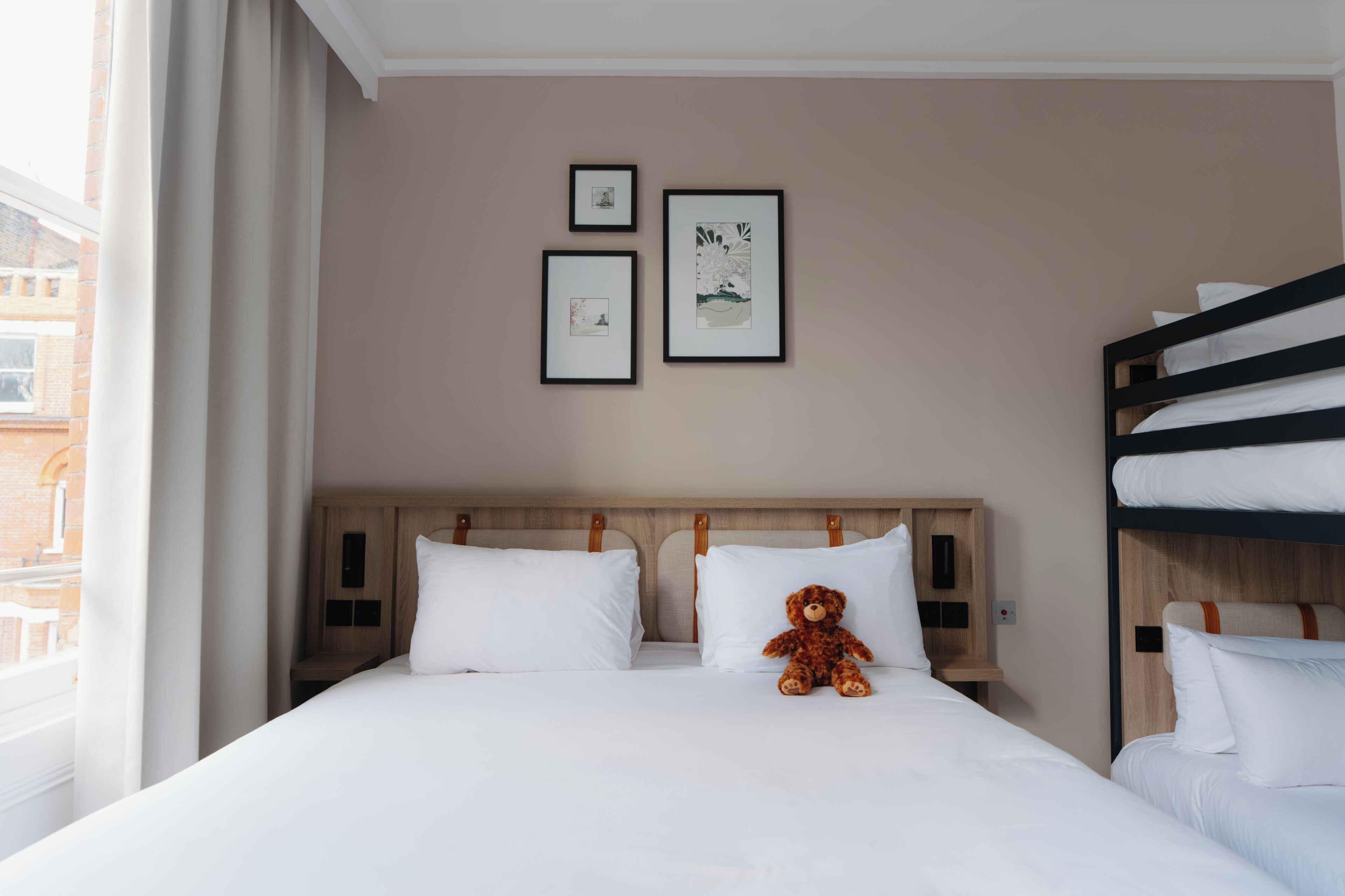 Hotellihuone, jossa on sänky, pehmolelu ja kaksi kehystettyä kuvaa seinällä.