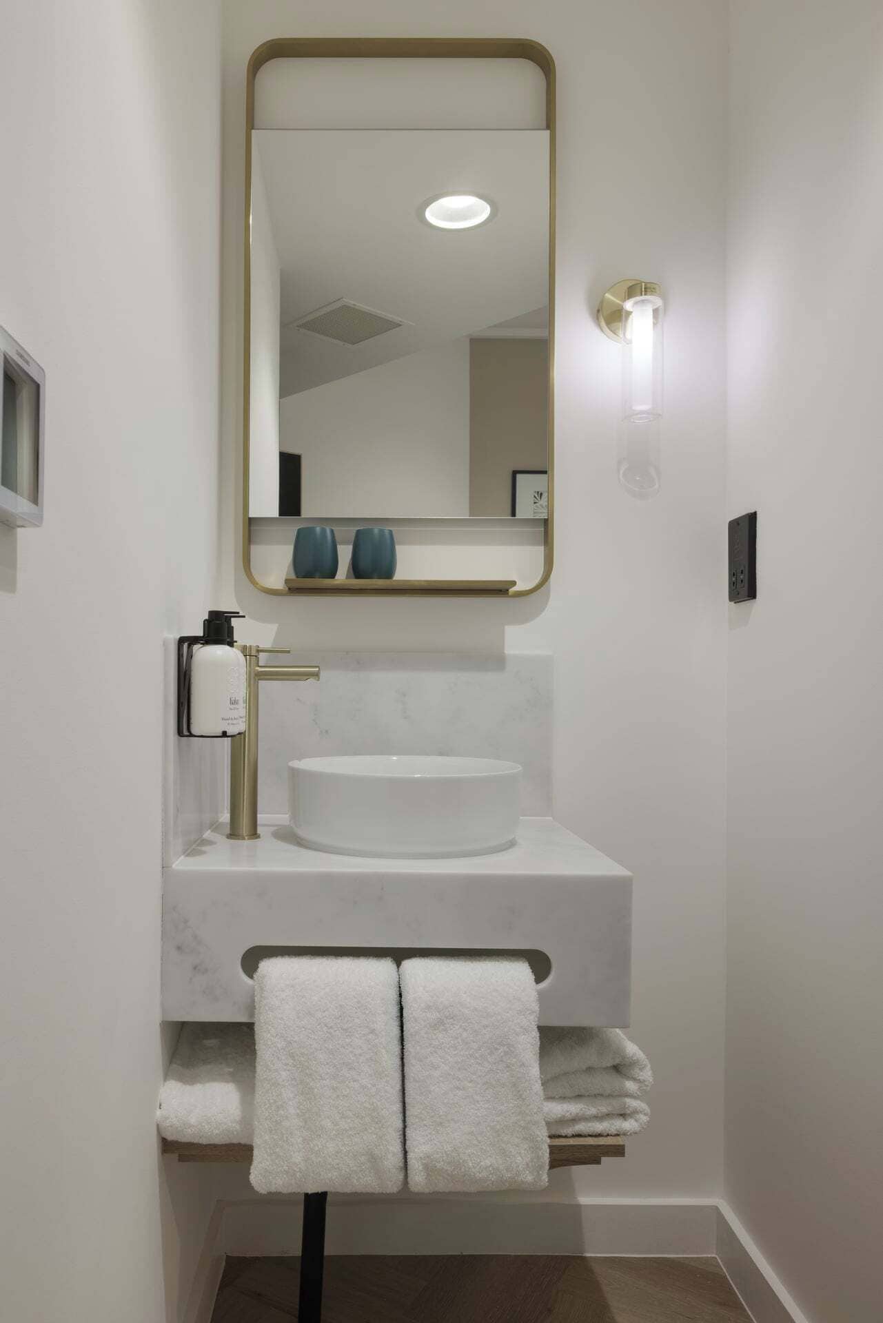 Ein modernes Badezimmer mit einem weißen Waschbecken, goldenen Armaturen und einem großen Spiegel.