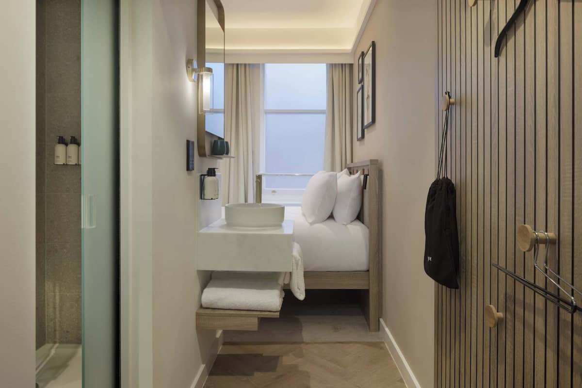A compact hotel room with a bed, a small bedside table, a mirror, and a wardrobe.