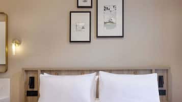 Ein Hotelzimmer mit einem Bett, zwei Kissen, einem Nachttisch, einer Wandlampe und drei gerahmten Bildern an der Wand.