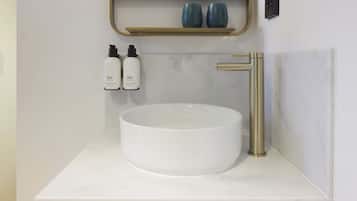 Ein Badezimmer mit Waschbecken aus weißem Marmor, Wasserhahn in Goldfarbe und zwei Flaschen Duschgel und Lotion auf einem Regal.