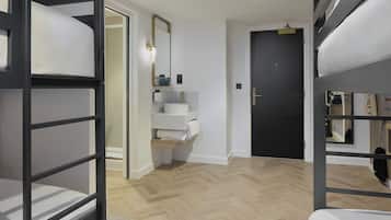 Una habitación de hotel moderna con literas, un baño con lavamanos y espejo, y una puerta que da a otra habitación.