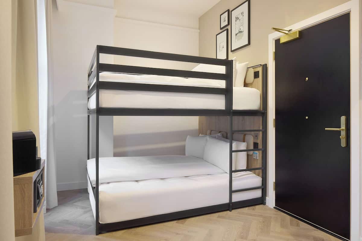 A bunk bed with a desk and chair, a black door, and a small shelf with books.