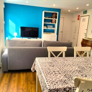 A room with a grey sofa, a TV, a white bookshelf, and a patterned table.
