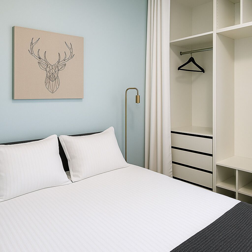 A neatly made bed with white linens, a hanging coat rack, and a wall-mounted artwork of a deer head.