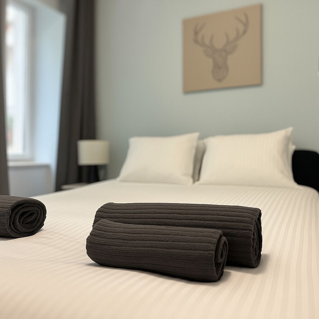 A neatly made bed with rolled towels, a lamp, and a deer head artwork on the wall.