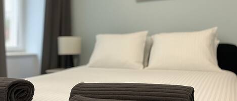 A neatly made bed with rolled towels, a lamp, and a deer head artwork on the wall.