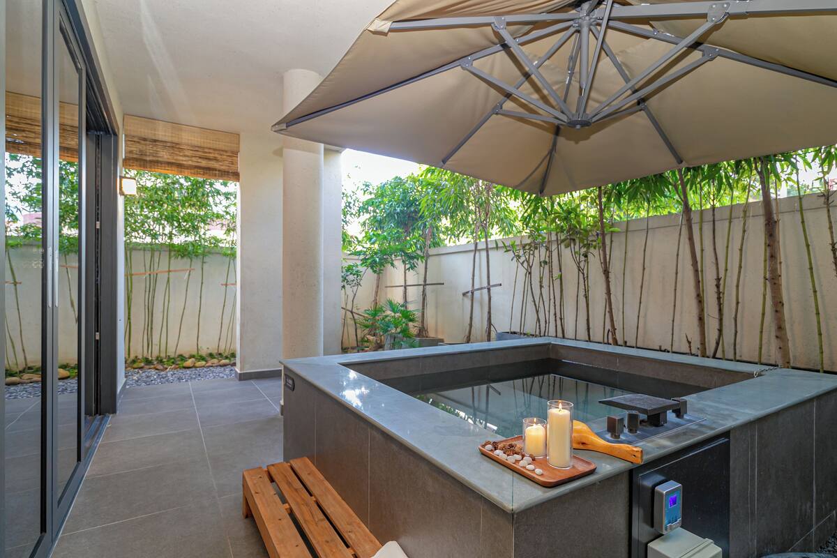 An outdoor kitchen area with a built-in stove, a wooden bench, and an umbrella providing shade.