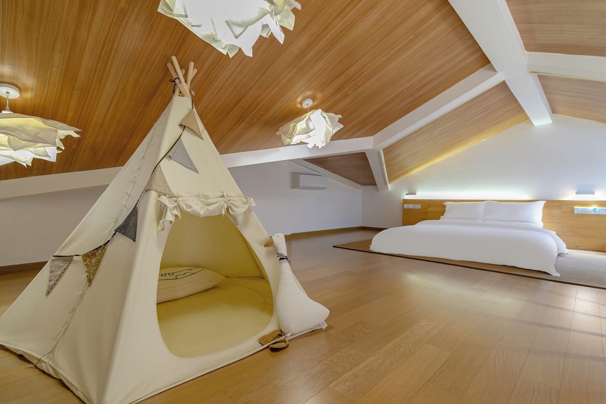 A cozy attic bedroom with a wooden ceiling, a white bed, and a small tent-like structure.
