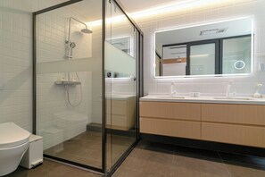 Un baño moderno con ducha envuelta en vidrio, inodoro blanco y tocador con espejo.