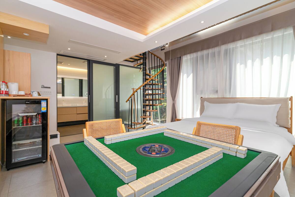 A hotel room with a bed, a minibar, a green carpet, and a bookshelf.