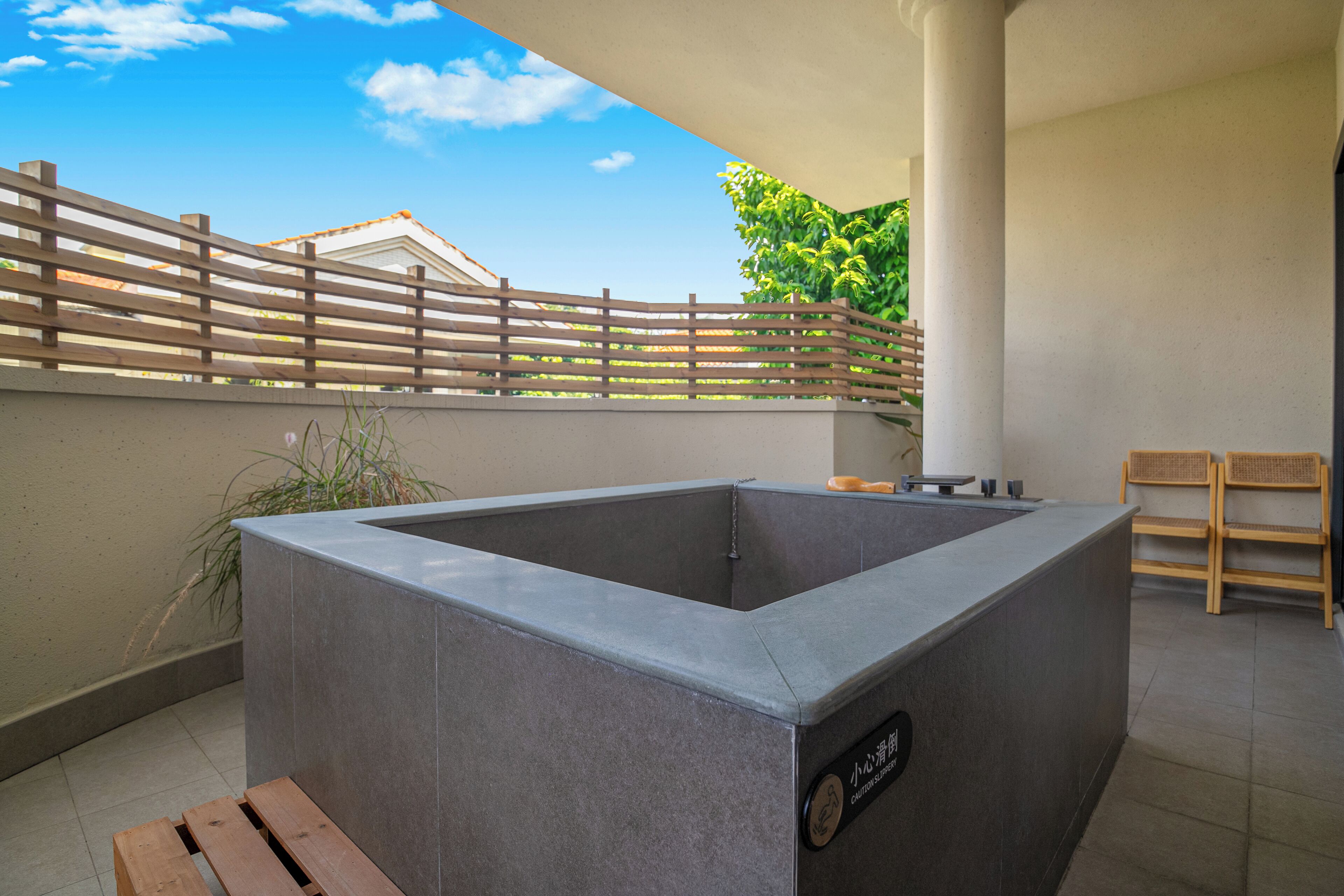 A modern outdoor hot tub area with a wooden fence, a bench, and a caution sign.