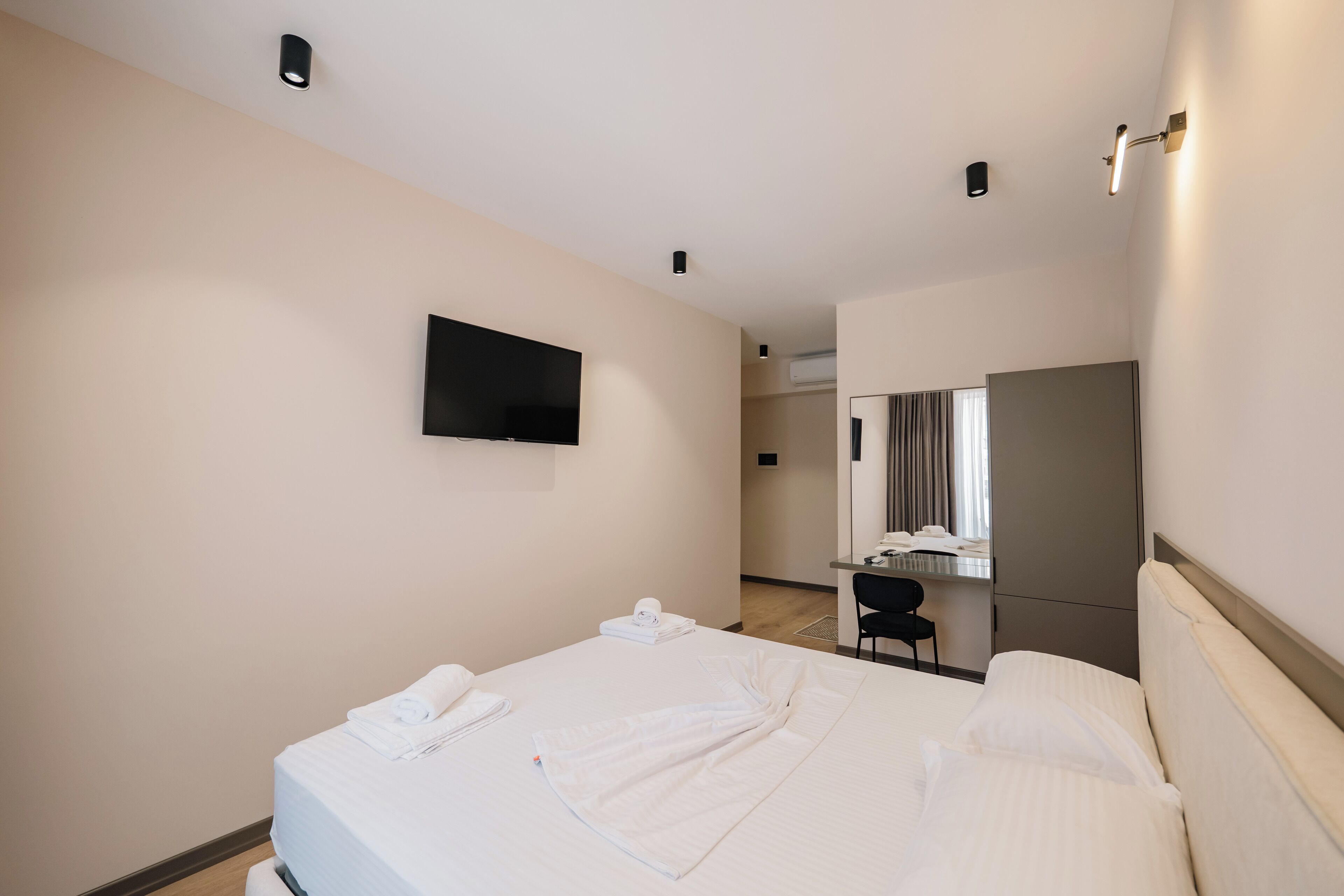 Una camera d'hotel con un letto, una TV a schermo piatto montata a parete, una scrivania con una sedia e uno specchio.